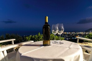 A table with a wine bottle and two glasses, set against a night view of a cityscape. - Rhapsody Traditional Apartments (Santorini)