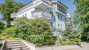 A multi-story building with balconies, surrounded by greenery and a staircase leading to the entrance. - Villa Sabinium 01: Close to the beach in Heringsdorf with your own beach chair (Heringsdorf (Seebad))