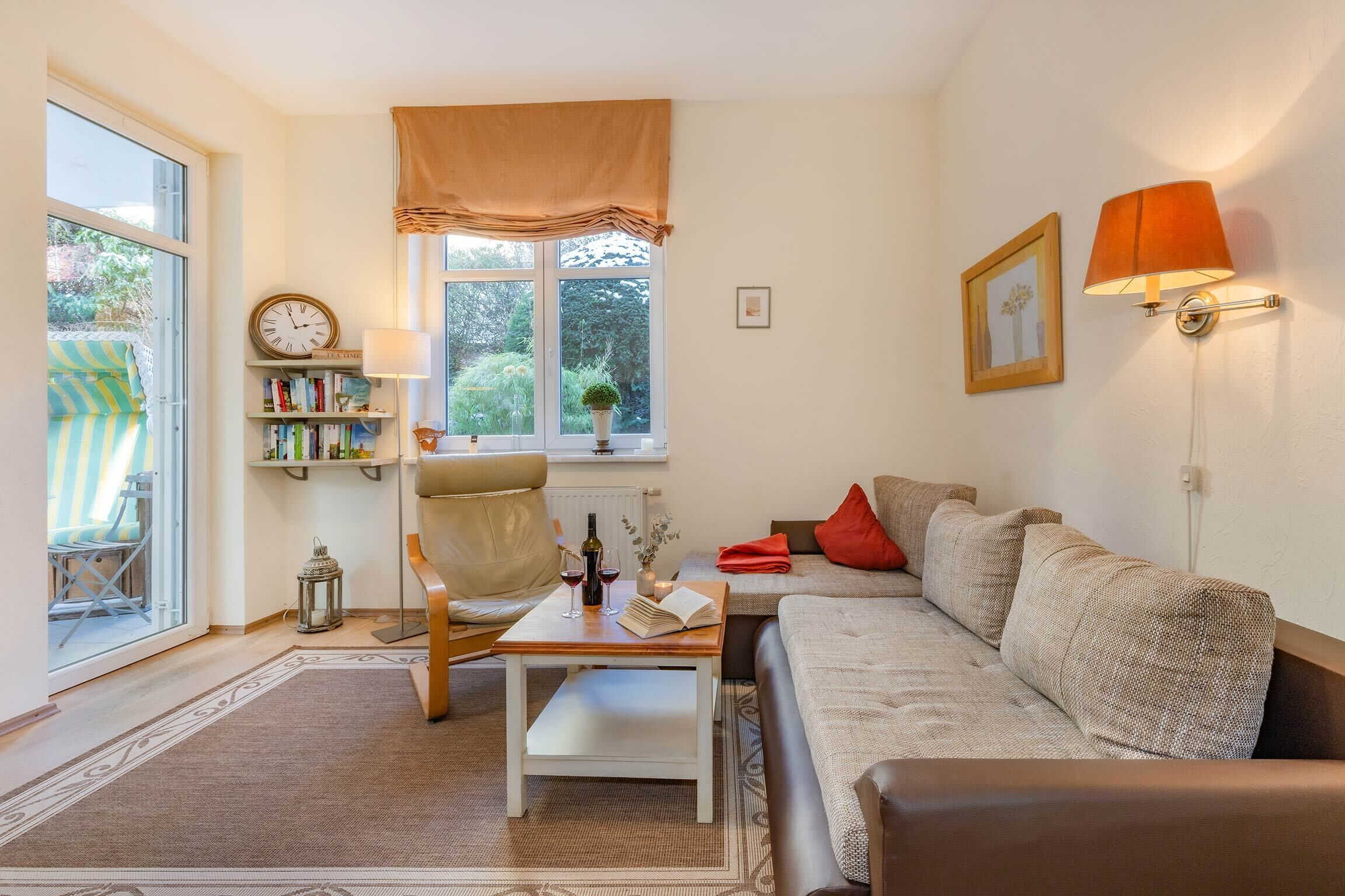 A cozy living room with a sofa, a coffee table, a bookshelf, and a window with a view of greenery.