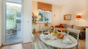 A dining area with a table set for breakfast, a sofa, and a window with curtains. - Villa Sabinium 01: Close to the beach in Heringsdorf with your own beach chair (Heringsdorf (Seebad))