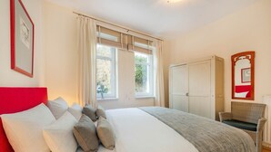 A bedroom with a bed, pillows, a window with curtains, a wardrobe, and a chair. - Villa Sabinium 01: Close to the beach in Heringsdorf with your own beach chair (Heringsdorf (Seebad))