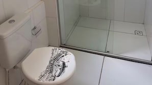 A bathroom with a glass shower enclosure, a toilet with a cityscape design, and white tiled walls. - Apartment for discerning people. (Barreiras)