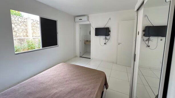 A room with a bed, a window, a TV mounted on the wall, and a door leading to another room. - Apartment for discerning people. (Barreiras)