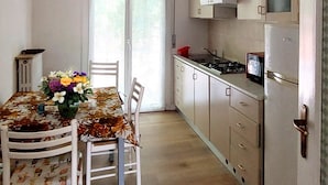 A kitchen with a dining table, chairs, a clock, cabinets, a stove, and a refrigerator. - CN028 - Cesenatico, Villa Federica - comfortable two-bedroom apartment with parking space (Cesenatico)