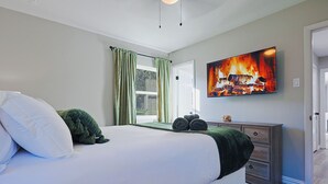 Ein Schlafzimmer mit einem großen Bett, einem Schminktisch, einem Flachbildfernseher und einem Fenster mit Vorhängen.