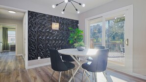 Ein Essbereich mit einer modernen, geometrischen Wand, einer Deckenleuchte und Blick ins Freie durch eine Glastür.