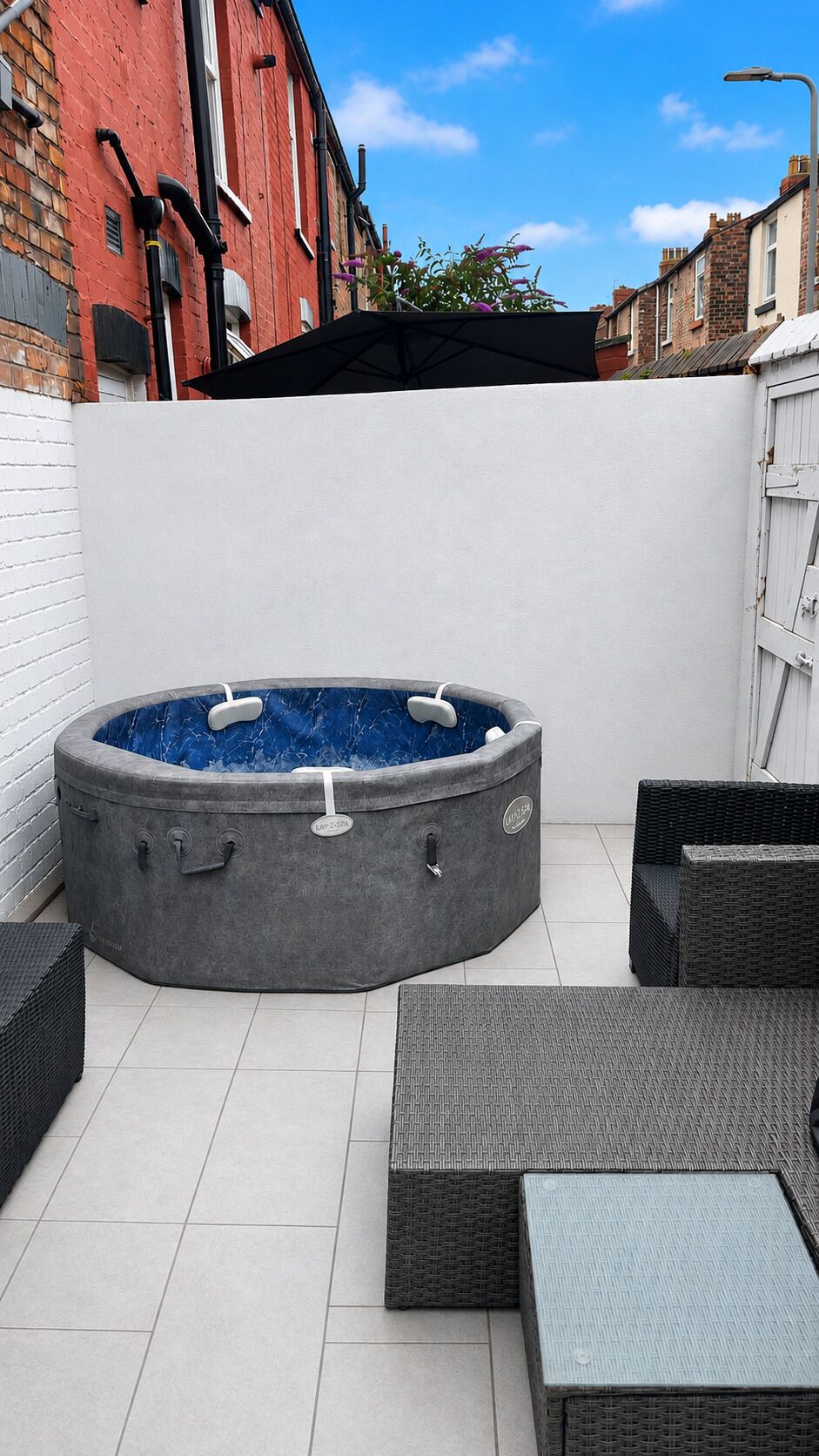 Un jacuzzi en un patio con suelo de baldosas y mobiliario de mimbre.