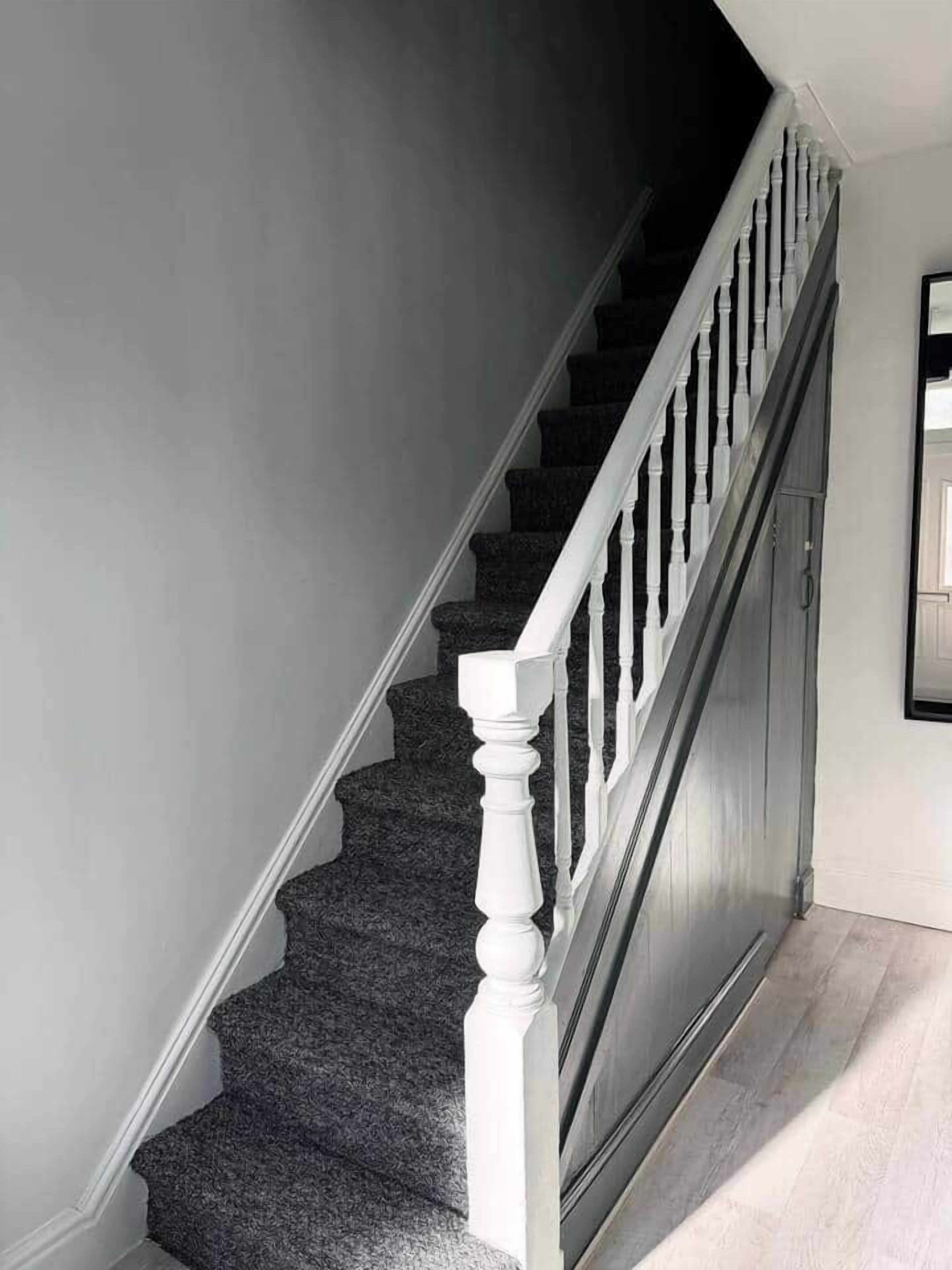 Un escalier avec des marches recouvertes d’une moquette sombre et des balustrades blanches.