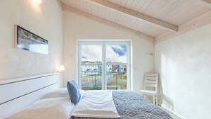 Et soveværelse med seng, stol, et vindue og udsigt til huse.
