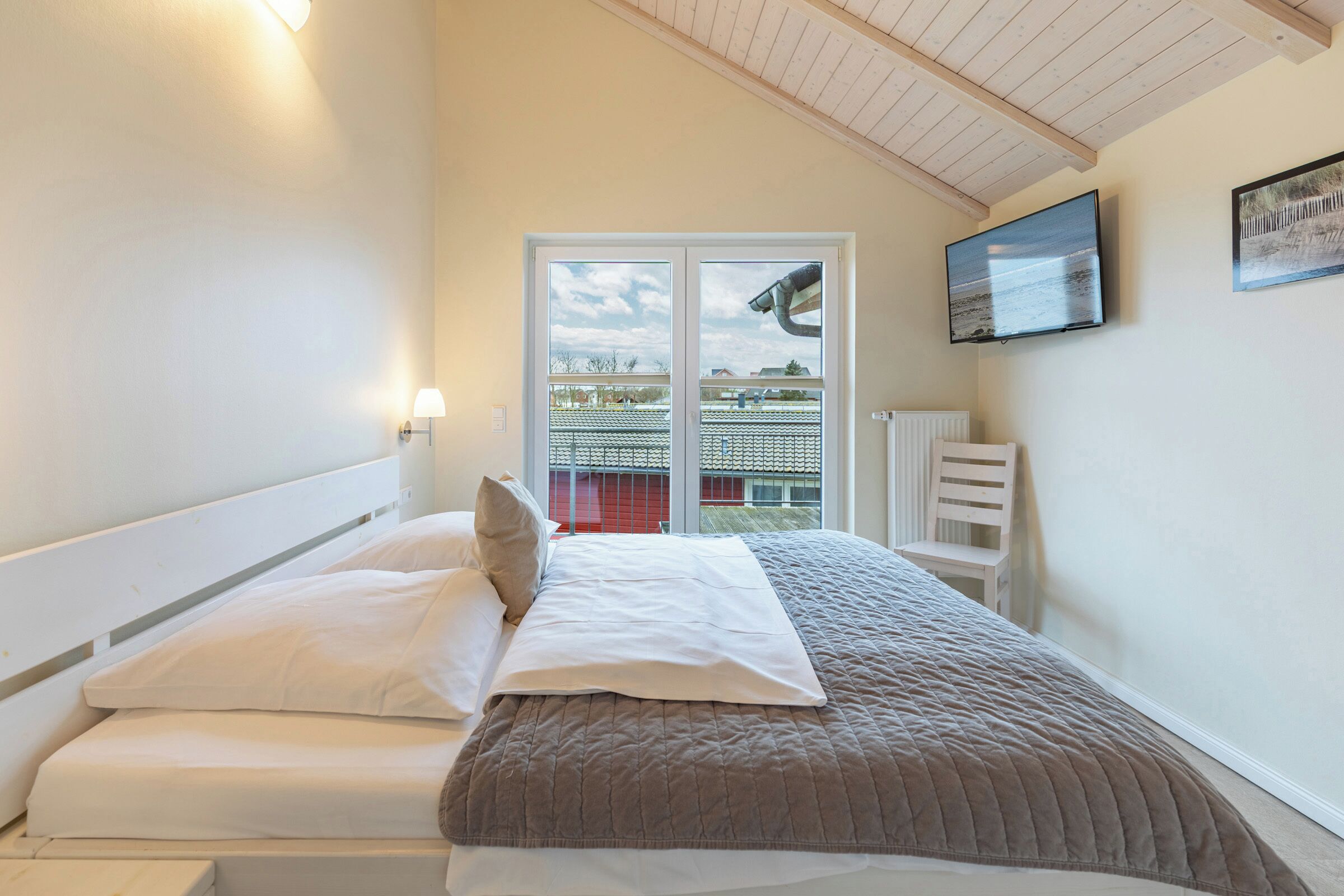 Ein Schlafzimmer mit Bett, Fenster, Fernseher und Heizkörper.