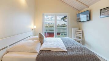 Ein Schlafzimmer mit Bett, Fenster, Fernseher und Heizkörper.