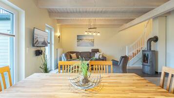Ein Essbereich mit Holztisch, Stühlen und einer Pflanze als Mittelpunkt. Im Hintergrund befinden sich eine Couch und eine Treppe.
