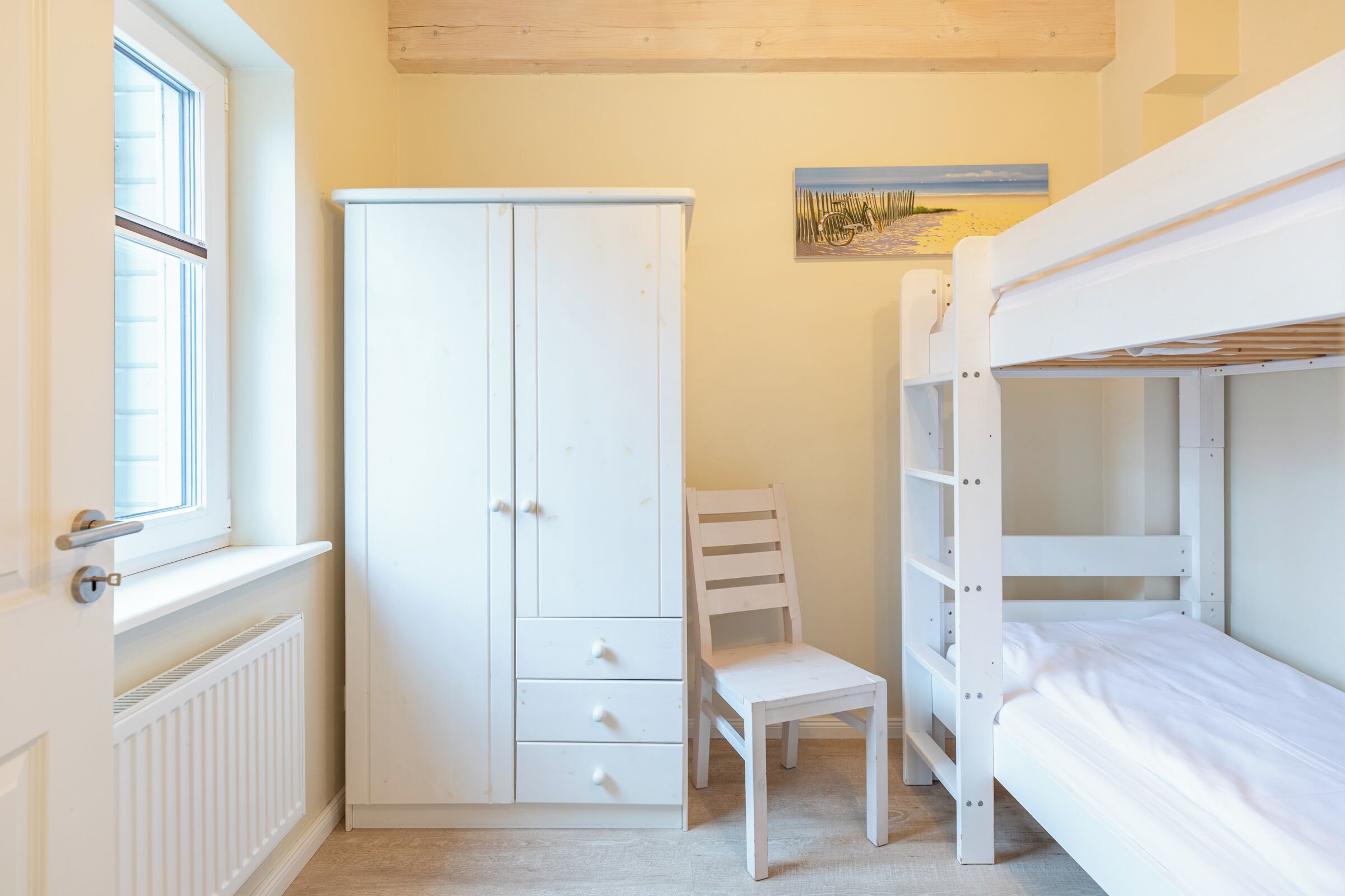 Ein Schlafzimmer mit Etagenbett, weißem Kleiderschrank, Stuhl und Heizkörper.