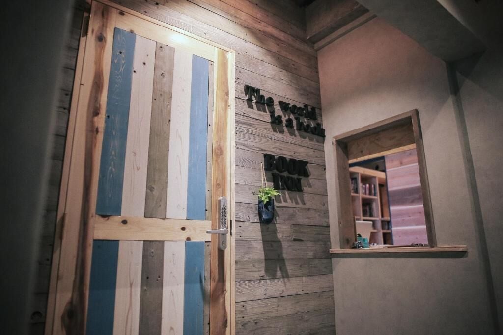 A wooden door with blue and white stripes, a small window with a shelf, and a wall with the text "The world is a book" and "BOOK IN".