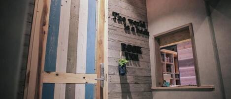 A wooden door with blue and white stripes, a small window with a shelf, and a wall with the text "The world is a book" and "BOOK IN".
