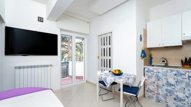 Una habitación compacta con cama, una mesa de comedor con sillas, una zona de cocina y un televisor en la pared.