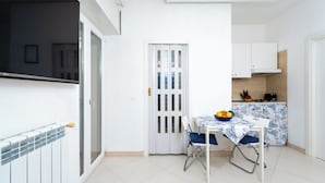 Una cocina compacta con comedor, armarios blancos y suelo de baldosas.