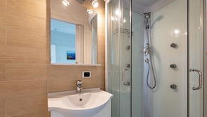 Un baño moderno con ducha acristalada, lavabo blanco y espejo sobre él.