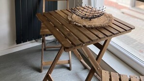 Un tavolo di legno con un cesto intrecciato e una sedia in una stanza con un pannello verticale scuro e una finestra dotata di persiana a rullo.