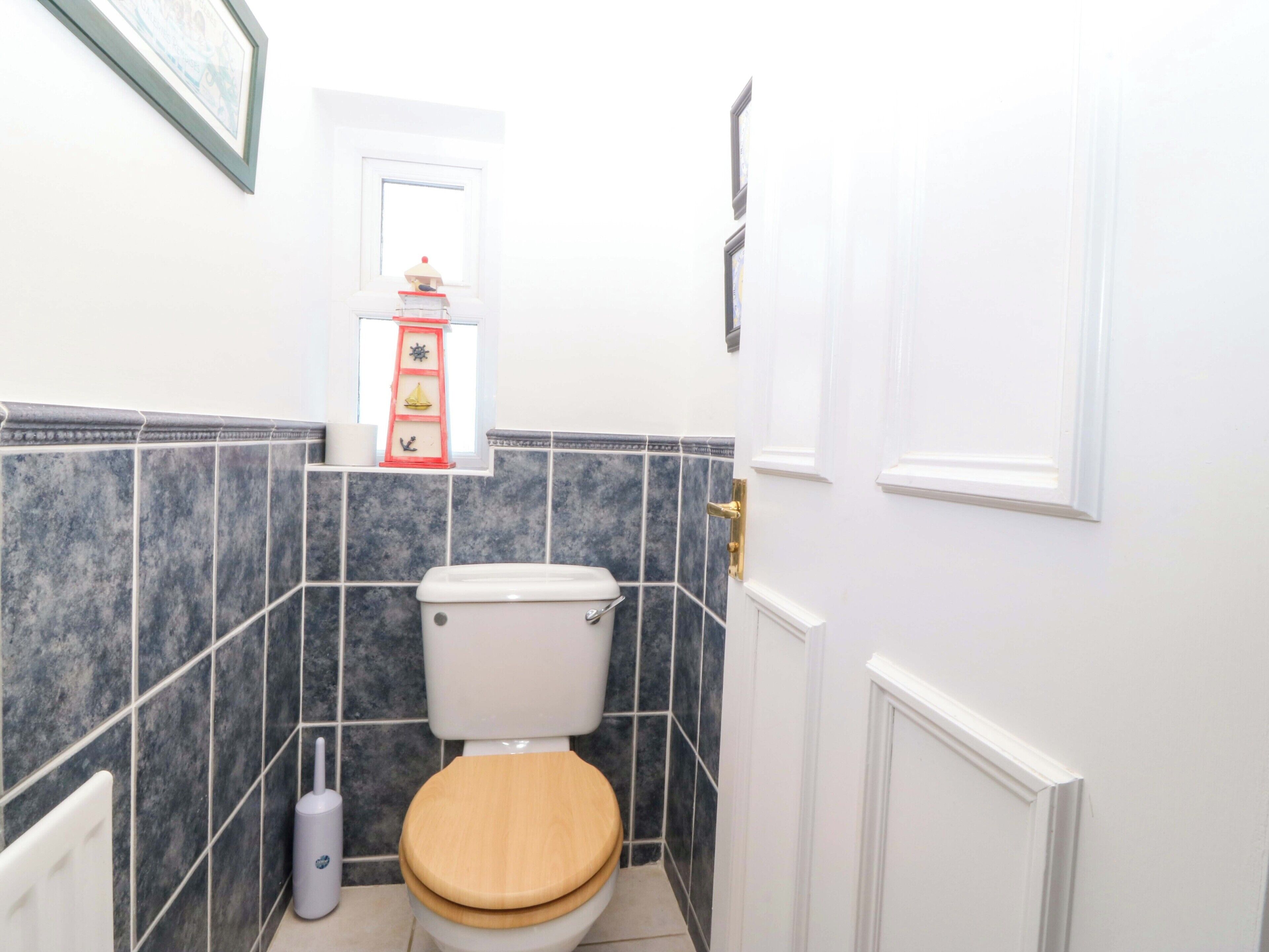 A bathroom with a toilet, a hand dryer, and a shelf with decorative items.