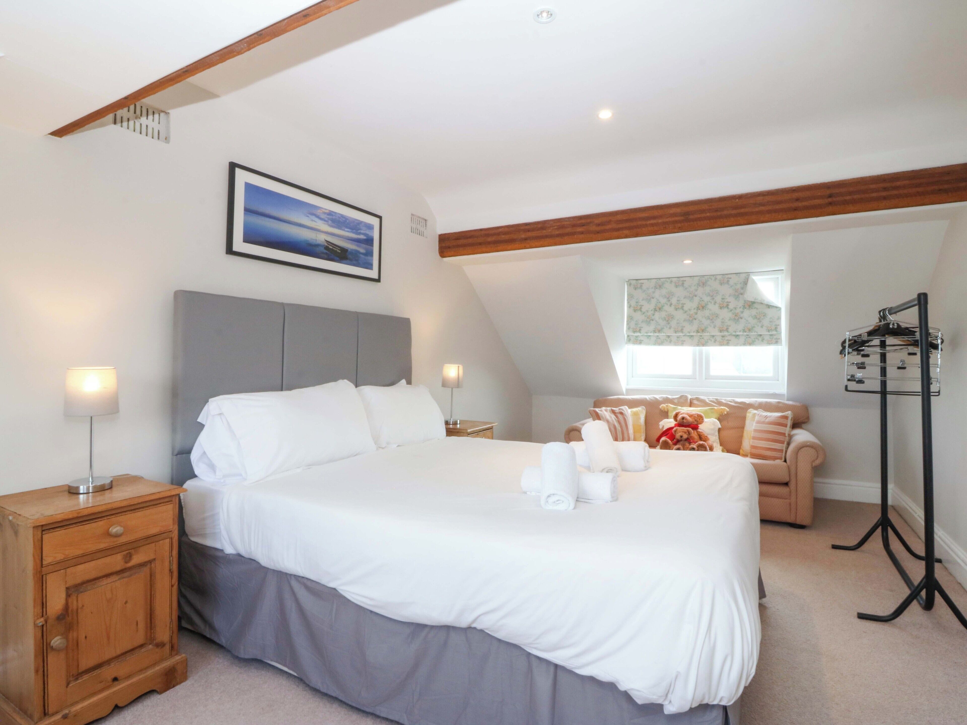 A bedroom with a large bed, bedside tables, a nightstand, a window with a view, and a hanging coat rack.