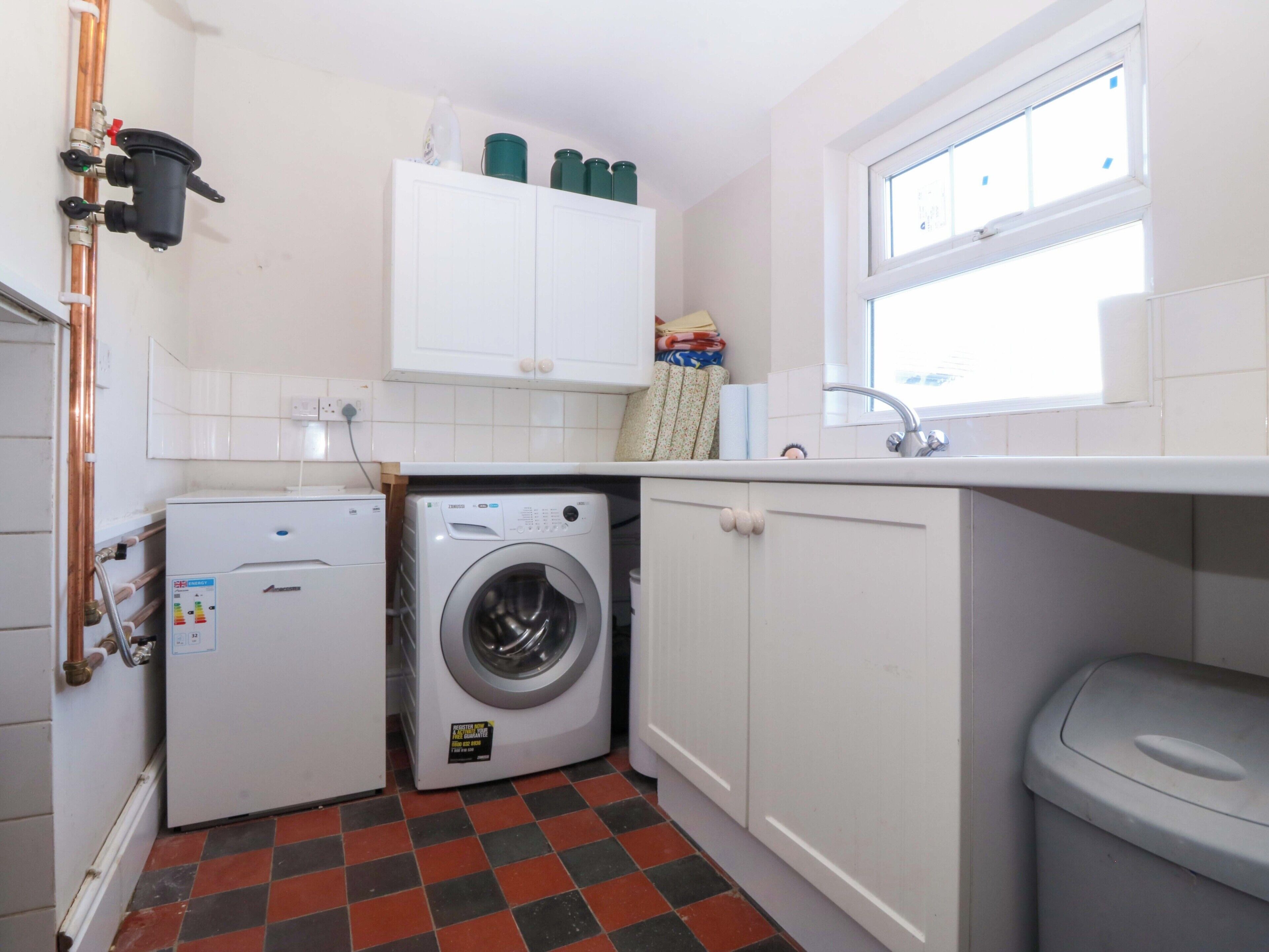 A compact laundry room with a washing machine, a dryer, a sink, and a window.