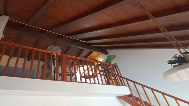 Uma escada de madeira com corrimão, um ventilador de teto e um vaso de planta.