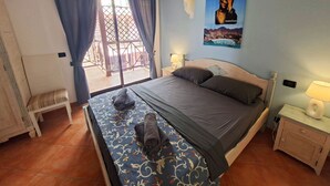 Quarto com cama, um banquinho, mesa de cabeceira, luminária e um pôster na parede.