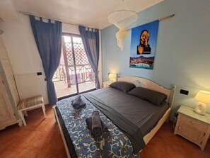 Ein Schlafzimmer mit einem Bett, einer Sitzbank, einem Nachttisch, einer Lampe und einem Bild an der Wand.