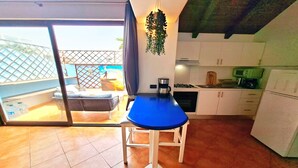 Uma cozinha compacta com uma mesa azul, armários brancos e uma planta pendente.