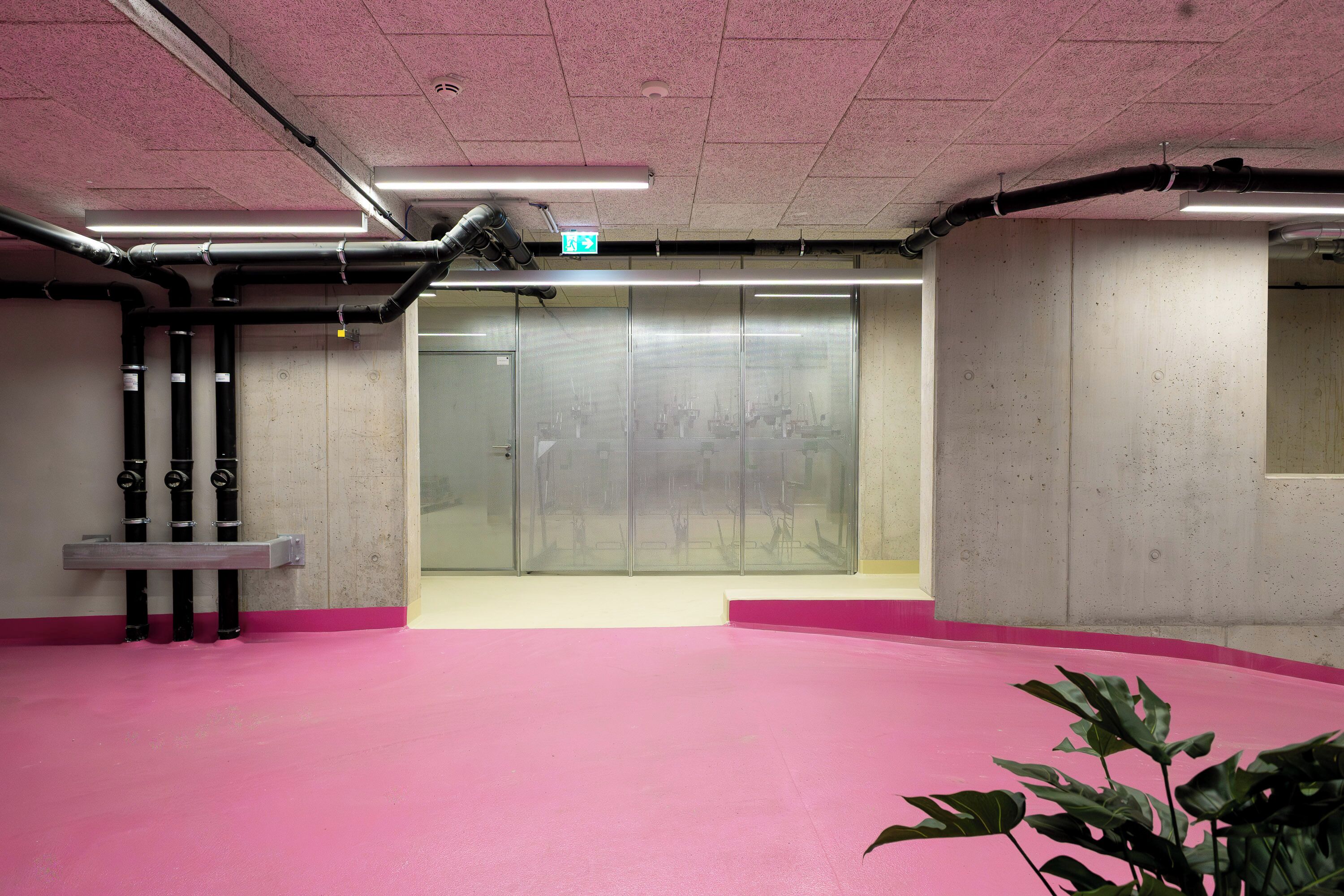 Et rummeligt indendørs område med pink gulv, betonvægge og en dør til en glas elevator.