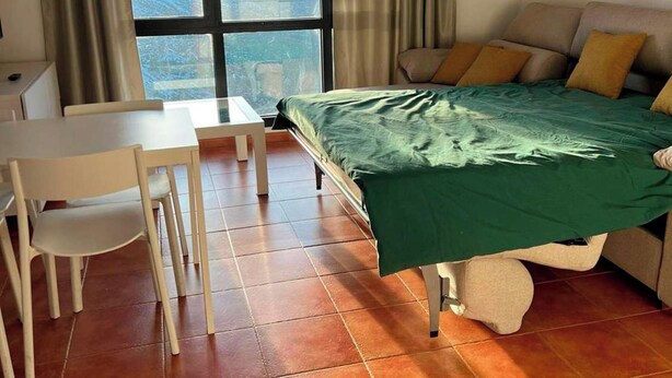 Una habitació amb un llit, un escriptori i una cadira. Hi ha una finestra amb cortines i un quadre a la paret.