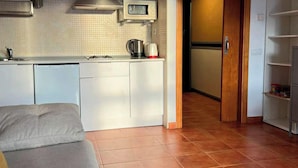 Un espai vital reduït amb una cuineta, un sofà i una porta que dona a una altra habitació.