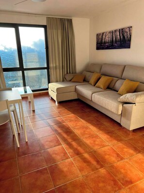 A living room with a sectional sofa, a dining table with chairs, and a large window with curtains. - Group Getaway Near Ski Slopes (Monachil)