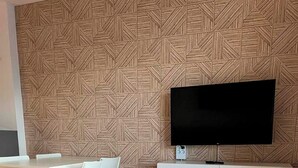 Un saló modern amb una paret amb un dibuix geomètric, un televisor de pantalla plana muntat sobre un moble blanc i una taula de café amb tapa de vidre.