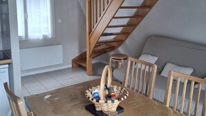 Een houten eettafel met stoelen, een mand met toevoegingen, een trap en een bed met kussens.