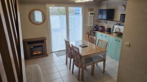 Een gezellige woonkamer met een open haard, een eettafel met stoelen, een keuken met een televisie, en een schuifpui naar een balkon.