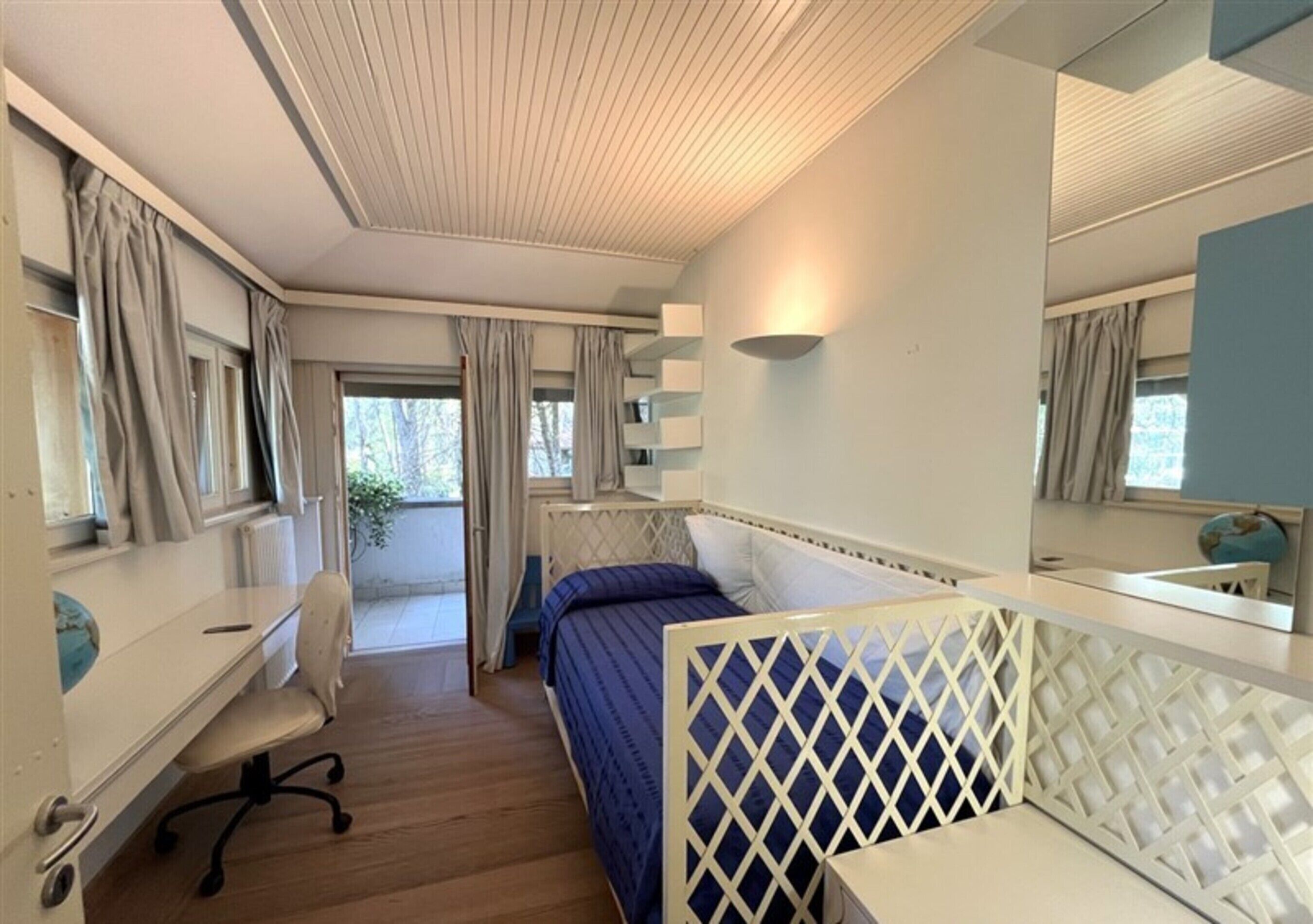 Een slaapkamer met een bed, een bureau en een stoel. Er is een raam met gordijnen, een radiator en een wereldbol op het bureau.