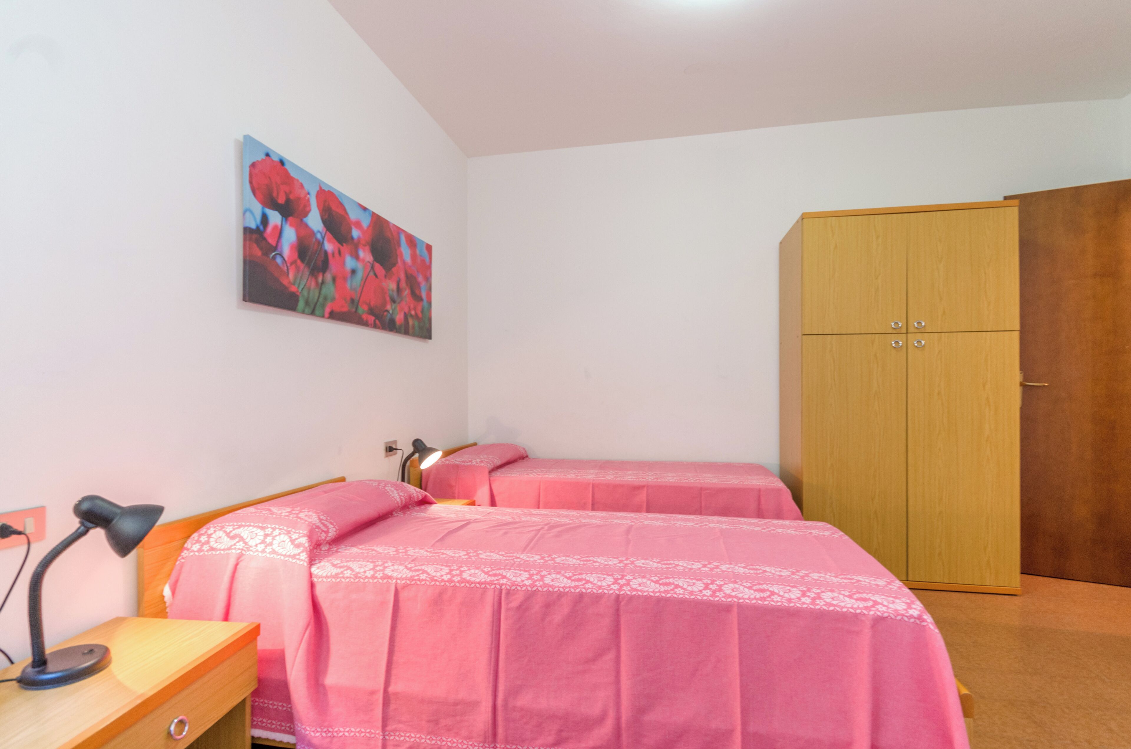 Ein Schlafzimmer mit zwei Betten, einem Holzschrank, einem Schreibtisch mit Lampe und einem Bild an der Wand.