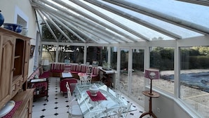 A conservatory with a glass table and chairs, a sofa, and a cabinet. - Old Maison de Maitre with great comfort (Gujan-Mestras)