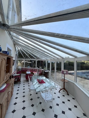 A conservatory with a glass table and chairs, a sofa, and a cabinet. - Old Maison de Maitre with great comfort (Gujan-Mestras)