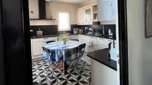 A modern kitchen with a dining area, featuring geometric patterned flooring, white cabinetry, and a central island with seating. - Old Maison de Maitre with great comfort (Gujan-Mestras)