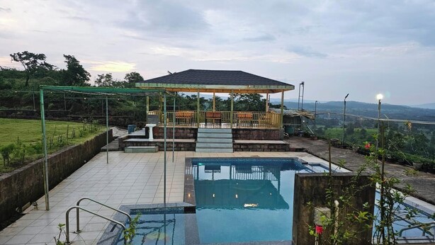 Uma piscina no terraço com um gazebo, cercada por um jardim e vista para as colinas.