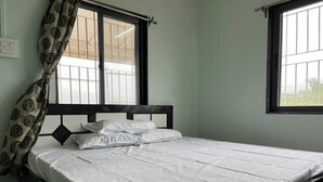 Uma cama de solteiro com colchão e almofadas brancos, cabeceira preta e janela com grade de metal.