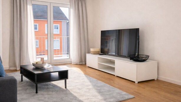 A modern living room with a flat-screen TV on a white stand, a black coffee table, and a grey rug. - Luxury apartment - Charming 2 room apartment (Augsburg)