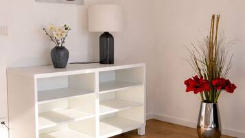 A white console table with a lamp and flowers, a gray rug, and a red abstract painting on the wall.