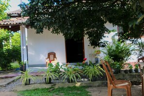 A covered outdoor area with a wooden chair, potted plants, and a building entrance. - Dihein surf Hostel (Ahangama)