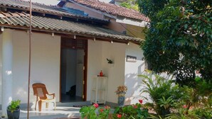Una casa con tetto in tegole, una porta d'ingresso, un piccolo portico, una sedia e piante in vaso.
