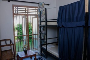 A dormitory room with bunk beds, a small table with a plant, and a view of greenery through a window. - Dihein surf Hostel (Ahangama)