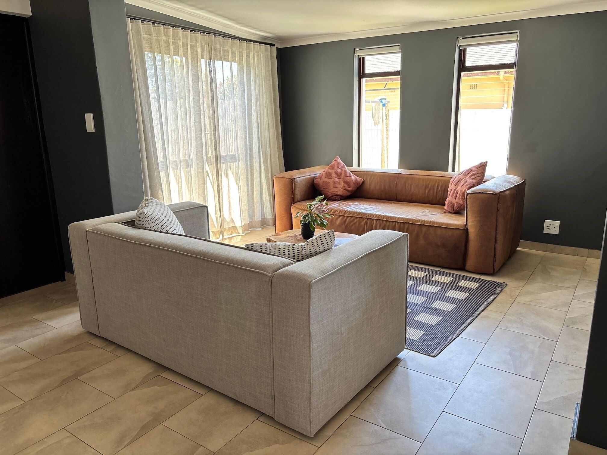 A living room with a beige sofa, a small coffee table, and a window with curtains.